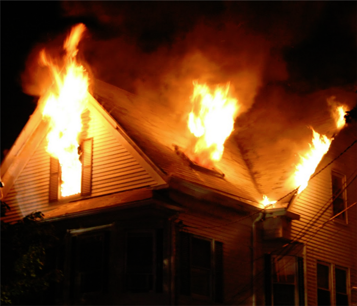 fire at night with flames coming out of the windows of a house