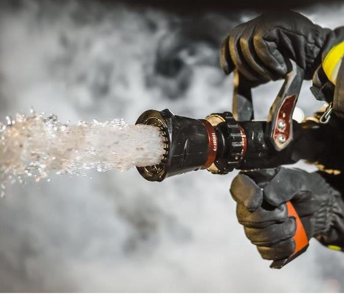 Closeup of fireman holding firehose; water rushing out of hose